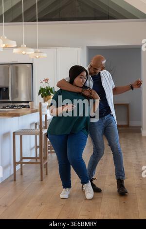 Afroamerikanisches Paar, das in der modernen Küche in der Nähe einer Holzinsel und einer Pflanze steht Stockfoto