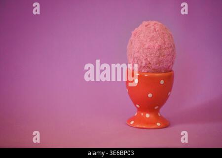 Rosafarbene Eiskugel in einer orangefarbenen Tasse mit Punktmuster vor einem weichen violetten Hintergrund für eine optisch ansprechende Dessertpräsentation Stockfoto
