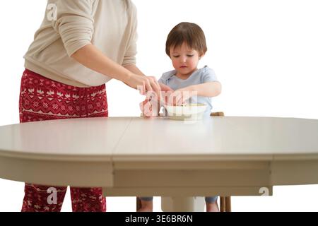 Frau, die Kind hilft, gesunden Gemüsesalat aus der Schüssel am Esstisch zu essen. Elternschaft und Fütterung von Kleinkindern zu Hause. Familienleben, Ernährung und h Stockfoto