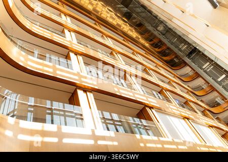 Ein flaches Bild eines modernen Atriums mit geschwungenen Holzbalkonen und einer Glasdecke. Sonnenlicht filtert durch das Oberlicht und hebt den Architekten hervor Stockfoto