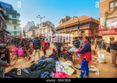 Fußgänger spazieren durch den lebhaften Open-Air-Straßenmarkt, gesäumt von Händlern und traditionellen Gebäuden in Kathmandu, Nepal Stockfoto