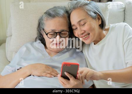 Fröhliche positive Erwachsene Tochter, die zusammen mit ihrer alten älteren Mutter zu Hause auf ein Handy schaut. Zeit miteinander verbringen. Happy Mother's d Stockfoto