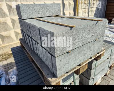 Stapel grauer Betonpflastersteine auf Holzpaletten, die für den Bau bereit sind Stockfoto