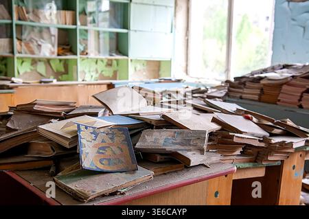 Ukraine, Pripyat, Tschernobyl-Ausschlusszone: Chaotische Anhäufungen von staubigen alten sowjetischen Lehrbüchern und Kinderbüchern auf Schreibtischen und auf dem Boden in heruntergekommenen elementaren en en Stockfoto