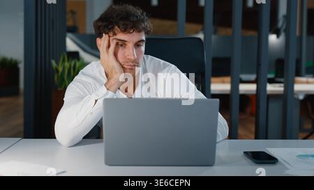 Langweiliger, müder kaukasischer Geschäftsmann, der sich langweilig fühlt, in Laptop zu schauen, unmotivierter Geschäftsmann männlicher Arbeiter, der mit dem Computer arbeitet Stockfoto