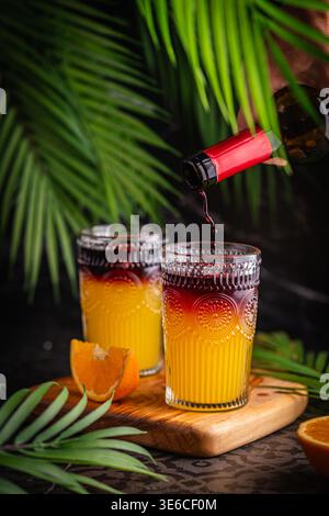 Ein Glas Cocktail mit Orangensaft und Rotwein oder frischer Sangria vor dunklem tropischen Hintergrund. Hochwertige Fotos Stockfoto