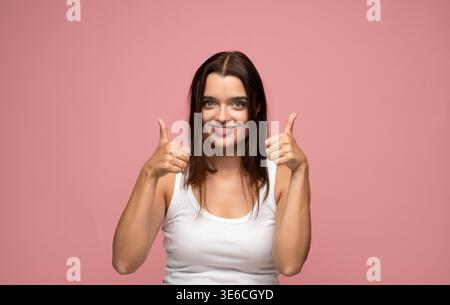 Frau, die zwei Daumen hochlegt, mit Zustimmung lächelt, Erfolg und Zufriedenheit zeigt. Positive Geste, gute Laune Stockfoto