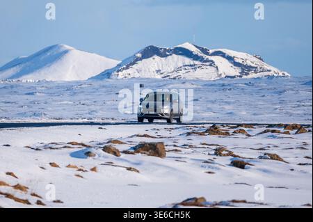 Auto fährt durch die verschneite Winterlandschaft in Island, Straßenfahrt bei kalter Witterung unter klarem blauem Himmel Stockfoto