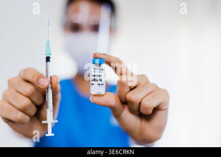 Medizinischer Mitarbeiter hält COVID-19-Impfstofffläschchen in der Hand mit Schutzhandschuhen und Blauen Scrubs Stockfoto