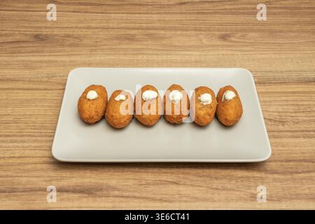 Eine Platte mit Kroketten in verschiedenen Geschmacksrichtungen: Etwas Schinken, etwas Huhn und etwas Käse, alle paniert und frittiert, bereit für ein Familienessen. Stockfoto