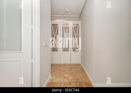 Undekoriertes minimalistisches Zimmer mit weißen eingebauten Kleidermodulen verschiedener Größen, einige mit soliden Türen und andere mit harmonischen Elementen Stockfoto