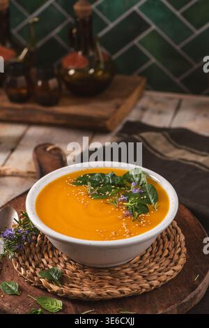 Eine lebendige Schüssel mit Orangengemüse wird mit frischem Spinat, Rosmarin und Sesamsamen garniert. Die warme, rustikale Küche bietet weiche Stockfoto