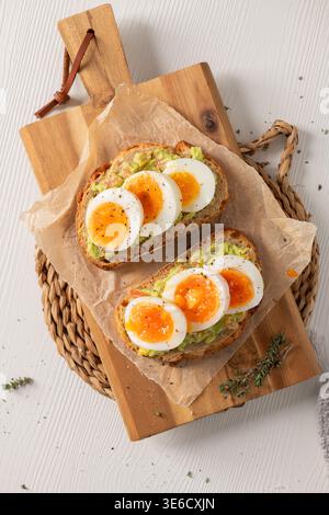 Zwei Scheiben gerösteter Sauerteig, belegt mit Avocadopüree und perfekt weichen gekochten Eiern. Die Szene ist hell und luftig mit natürlichem Lichtlicht Stockfoto