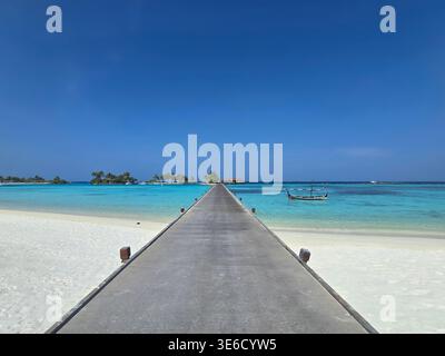 Ein langer Fußweg erstreckt sich vom weißen Sandstrand bis zur klaren türkisfarbenen Lagune und zeigt die Schönheit des Malediven Resort. Stockfoto