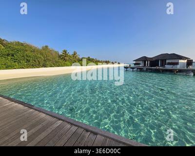 Genießen Sie einen luxuriösen Aufenthalt auf den Malediven mit Villen über dem Wasser, türkisfarbener Lagune und weißen Sandstränden unter klarem blauem Himmel. Stockfoto