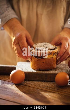 Hefeteig Cruffin Brötchen mit Mohnsamen und Succades Füllung. Zusammengerollte Brioche, Osterbacken. Eine Person in einer Schürze legt vorsichtig einen Kuchen auf eine Woo Stockfoto