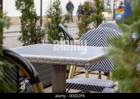 Nahaufnahme eines gemütlichen Cafés im Freien mit leeren schwarz-weiß gemusterten Korbstühlen und Tisch, die auf eine ruhige urbane Straßenszene hinweisen Stockfoto