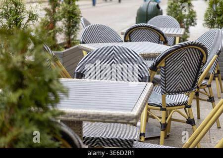 Detaillierte Ansicht der eleganten Cafétische und -Stühle im Freien, die das gemusterte Schwarz-weiß-Design hervorheben, ideal für einen charmanten europäischen Bürgersteig Stockfoto