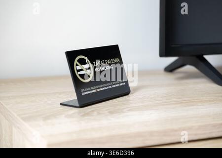 Nahaufnahme eines schwarzen „RAUCHVERBOT“-Richtlinienschildes auf einem hellen Holztisch, der klare Regeln bezüglich Unterkunft, Gesundheit und möglicher Gebühren für vermittelt Stockfoto