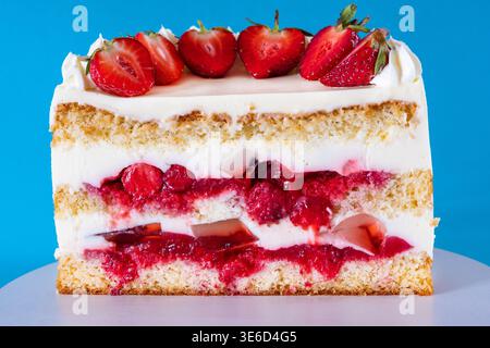 Eleganter hausgemachter Vanilleschwammkuchen, dekoriert mit frischen Erdbeerscheiben und Schlagsahnekäse. Hochwinkelaufnahmen auf dunklem Hintergrund, ideal für Stockfoto