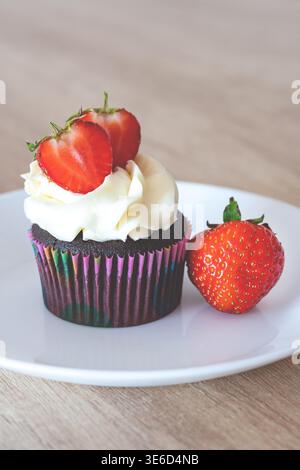Makroaufnahme eines köstlichen Vanille-Cupcake mit einem Schuss rosa Frischkäse-Frosting und einer frischen Erdbeerscheibe. Serviert auf einem weißen Teller Agave Stockfoto