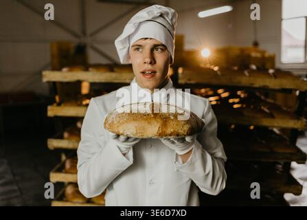 Junge glückliche Arbeiterin in sterilen Tüchern, die frisch gebackene Plätzchen auf Weißblech in der Lebensmittelfabrik halten. Stockfoto