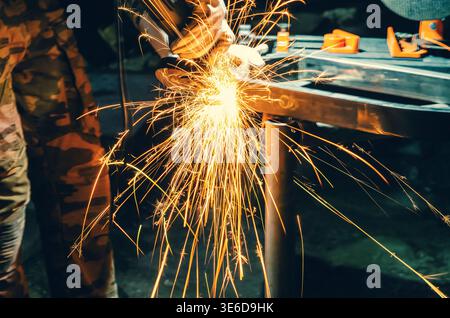 Goldene Funken beim Polieren von Metall in der Werkstatt. Dramatische Beleuchtung und unscharfer dunkler Hintergrund betonen Energie, Bewegung und industrielle Atmosphäre. Stockfoto