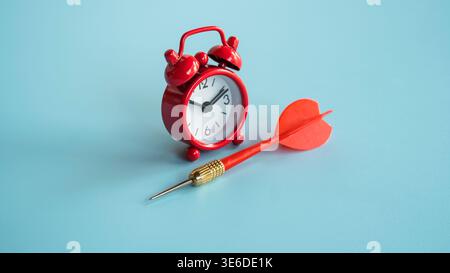Roter Wecker und roter Pfeil isoliert auf blauem Hintergrund für dringende Termine und Targeting. Stockfoto