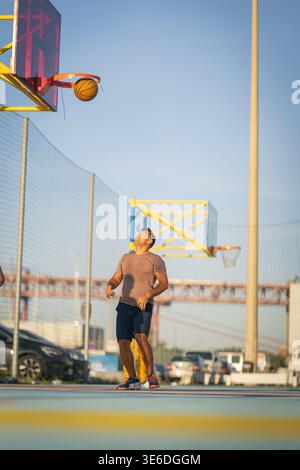 Der junge Mann konzentrierte sich auf Basketball, der auf einem farbenfrohen Outdoor-Court durch den Basketball ging Stockfoto