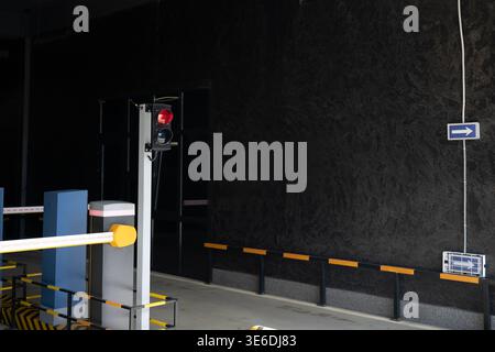 Eingang zu einer Tiefgarage mit Sicherheitsbarriere, Ampel und Richtpfeilschild an einer dunklen strukturierten Wand. Stockfoto
