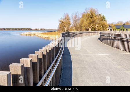 Weitwinkelaufnahme von einer Holzbrücke mit Blick auf einen ruhigen See und einen fernen Wald. Modernes Design, das sich mit der natürlichen Frühlingsumgebung verbindet. Stockfoto