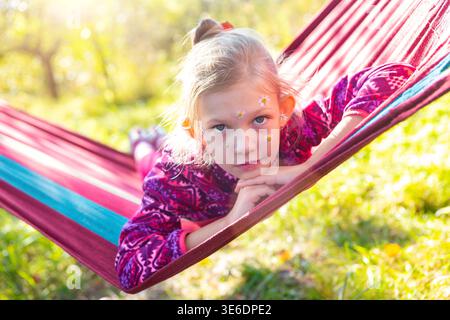 Das Kind entspannt sich in der Hängematte am sonnigen Tag im Garten mit Blumen im Gesicht Stockfoto