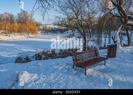 Moczydlo Park Winterlandschaft mit Bank am gefrorenen Teich bei Sonnenuntergang in Warschau, Polen. Stockfoto