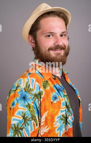 Studio-Porträt eines glücklichen bärtigen kaukasischen Mannes, der ein leuchtendes orangenes Aloha-Hemd und eine Strohfedora trägt. Perfekt für Sommerurlaub, Tourismus, Stockfoto