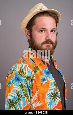 Studio-Porträt eines jungen kaukasischen Mannes mit Bart, der ein leuchtendes orangenes Aloha-Hemd und einen Strohhut trägt. Ideal für Sommerurlaub, Reisen, Stockfoto