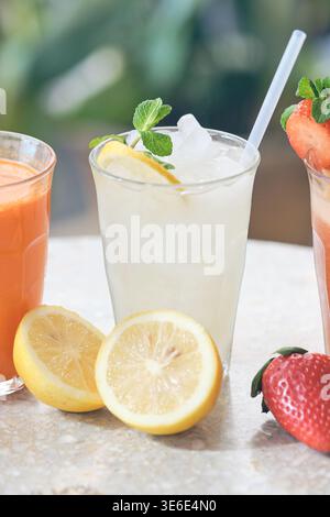 Gläser frischer Limonade, Karottensaft und Erdbeeren-Smoothie mit Obst auf einem Tisch Stockfoto