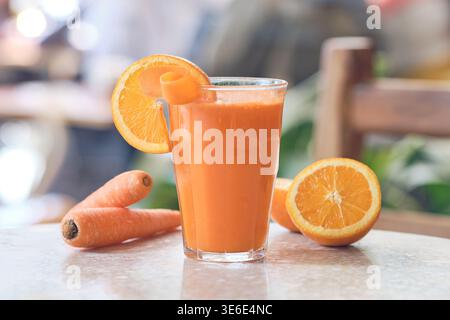 Glas hausgemachten Orangen- und Karottensaft mit einer Orangenscheibe und Schale auf einem Tisch Stockfoto