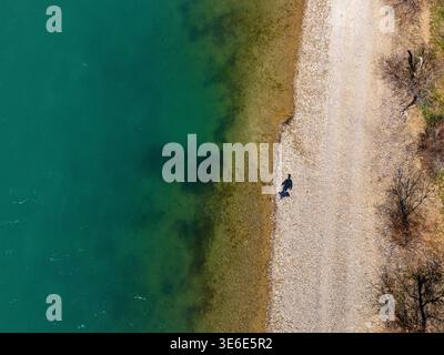 An einem sonnigen Tag spaziert der Mensch am Ufer eines Stausees entlang. Das türkisfarbene Flusswasser und der gelbe Sandstrand. Freizeitangebote im Freien. Stockfoto