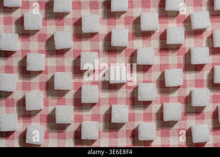 Zuckerwürfelmuster auf rosa Gingham-Tischdecke. Blick von oben auf weiße Zuckerwürfel, die im Gitter auf kariertem Stoff angeordnet sind. Konzeptbild für Süßigkeiten, Kalor Stockfoto