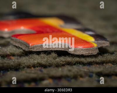 Detailliertes lebendiges Makroaufnahmebild des bunten roten orange gelben Puzzleteils, das auf strukturiertem Teppichhintergrund ruht Stockfoto