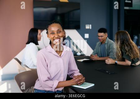 Lächelnder schwarzer Geschäftsmann mit einem vielfältigen Team während der Besprechung im Sitzungssaal im Büro tagsüber Stockfoto