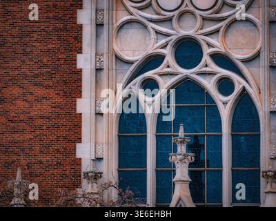 Gotische Kirchenfassade mit verziertem Steintrakt und blauem Buntglasfenster mit roter Backsteinfassade mit historischen architektonischen Details Stockfoto