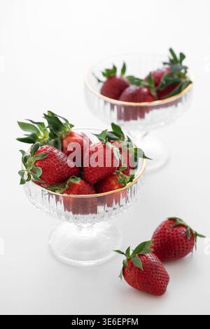 Elegante Komposition mit frischen roten Erdbeeren in dekorativen Glasschalen mit goldenen Rändern auf weißem Hintergrund Stockfoto