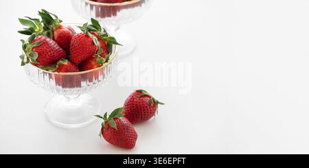 Elegante Komposition mit frischen roten Erdbeeren in dekorativen Glasschalen mit goldenen Rändern auf weißem Hintergrund Stockfoto