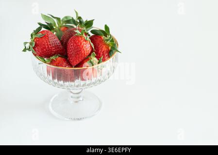 Elegante Komposition mit frischen roten Erdbeeren in dekorativen Glasschalen mit goldenen Rändern auf weißem Hintergrund Stockfoto