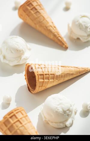 Minimalistische Sommerkomposition mit Waffeleiskegeln und Vanilleeis auf einem sauberen weißen Tisch. Stockfoto