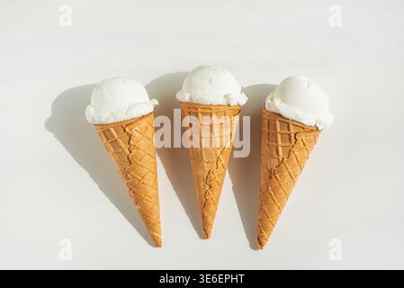 Minimalistische Sommerkomposition mit drei Waffel-Eiskegeln mit Vanilleeis auf einem sauberen weißen Tisch. Stockfoto