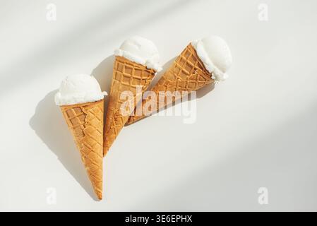 Minimalistische Sommerkomposition mit drei Waffel-Eiskegeln mit Vanilleeis auf einem sauberen weißen Tisch. Stockfoto