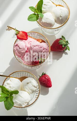 Elegante Komposition mit drei Glas-Dessertschalen mit goldenen Rändern, gefüllt mit Vanilleeis und Erdbeereis. Stockfoto