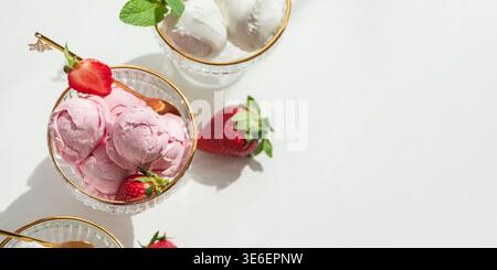 Elegante Komposition mit drei Glas-Dessertschalen mit goldenen Rändern, gefüllt mit Vanilleeis und Erdbeereis. Stockfoto